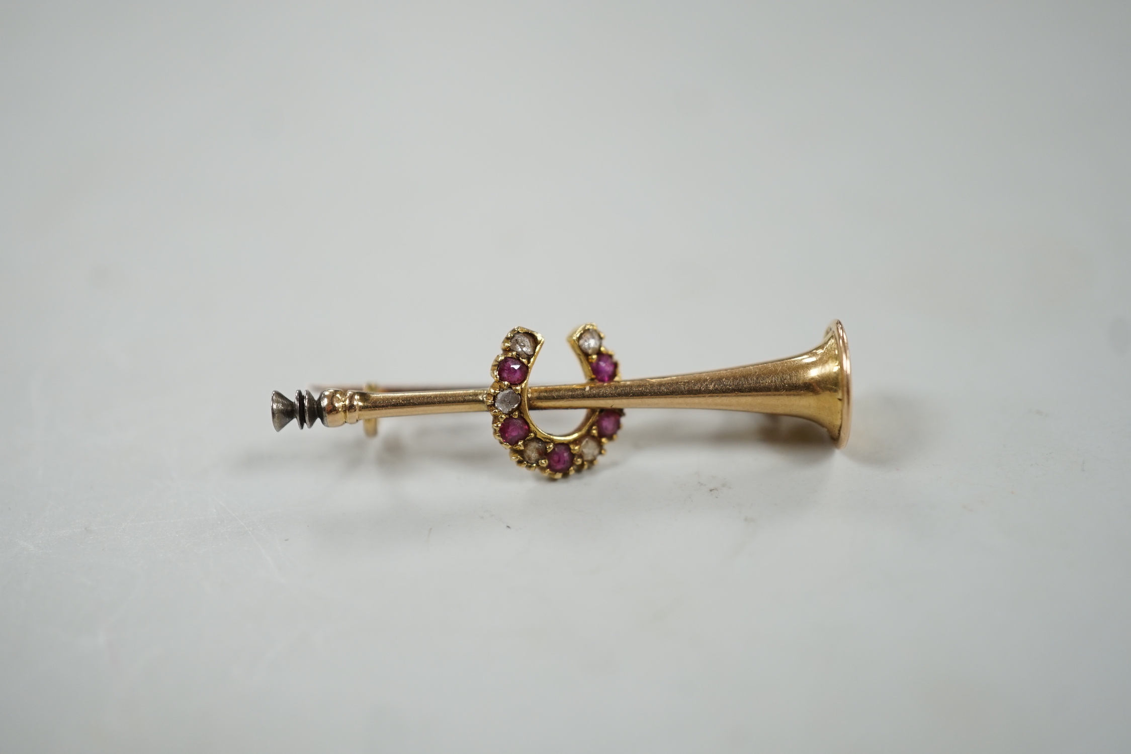 An Edwardian yellow metal, ruby and diamond set hunting horn and horseshoe brooch, 37mm, gross weight 2.6 grams.